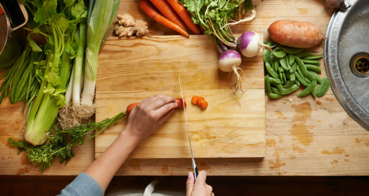 Person chopping carrot on wooden cutting board