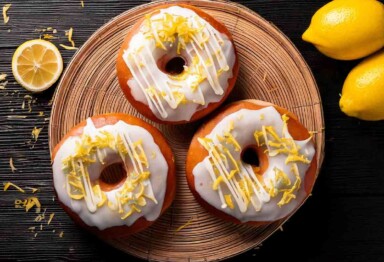 Overhead view of lemon ginger donuts on a round tray with surrounding lemon accents.