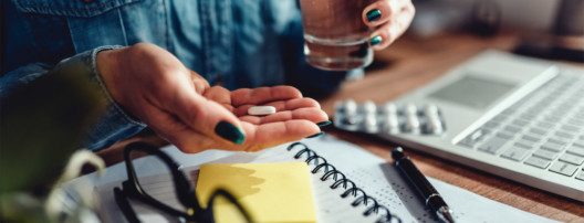 Woman holding pill in hand at desk