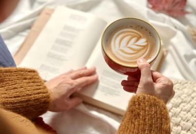 Woman holding a mug in while in bed reading a book