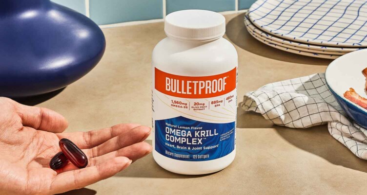 Hand holding bulletproof omega krill complex supplement next to bottle on counter