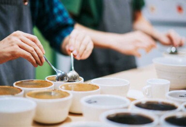 Cups of coffee on a table with the hands of a quality tester checking the coffee with 2 spoons