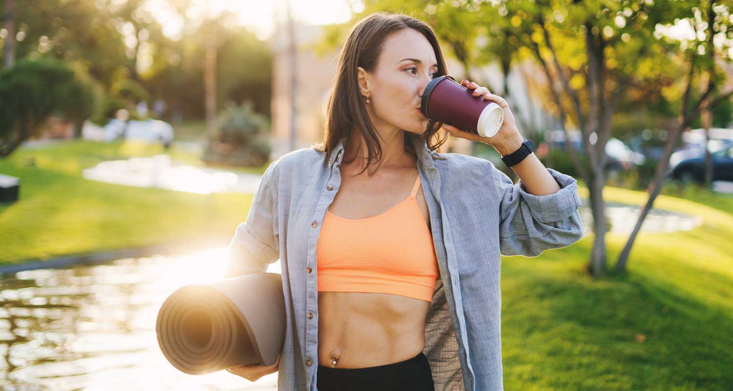 woman in workout clothing drinking coffee outside